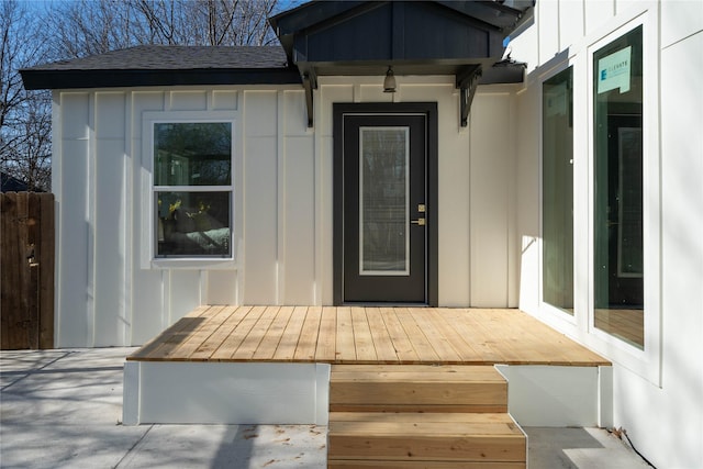 view of exterior entry featuring a deck, a shingled roof, and board and batten siding