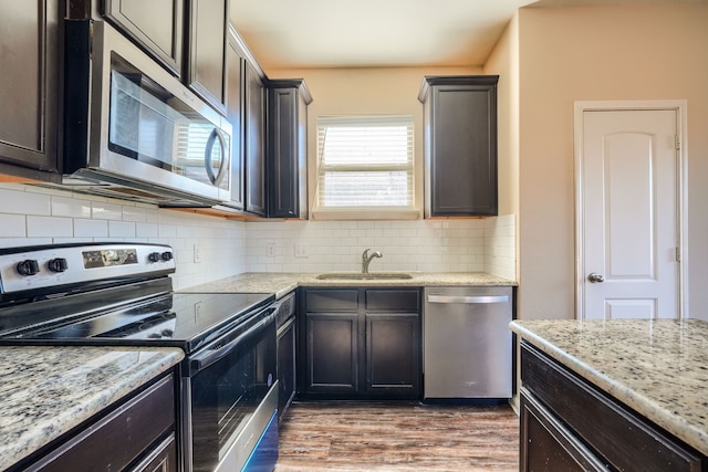 kitchen with sink, appliances with stainless steel finishes, dark hardwood / wood-style floors, light stone countertops, and decorative backsplash