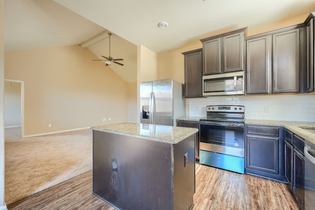 kitchen with appliances with stainless steel finishes, vaulted ceiling with beams, a center island, ceiling fan, and light stone counters