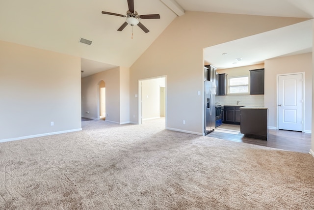 unfurnished living room featuring ceiling fan, high vaulted ceiling, beamed ceiling, and dark colored carpet