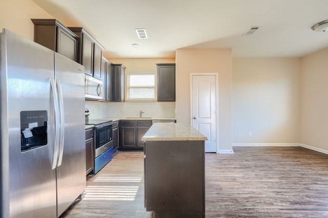 kitchen featuring tasteful backsplash, a kitchen island, stainless steel appliances, light stone countertops, and light hardwood / wood-style floors