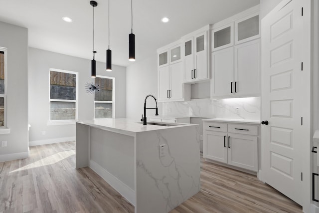 kitchen featuring sink, a kitchen island with sink, pendant lighting, and decorative backsplash