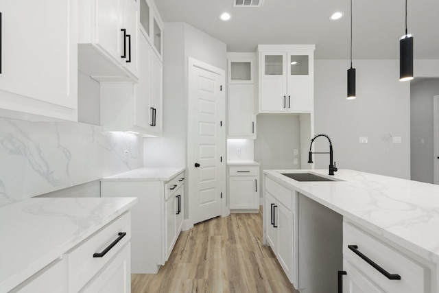 kitchen featuring light stone counters, sink, hanging light fixtures, and white cabinets