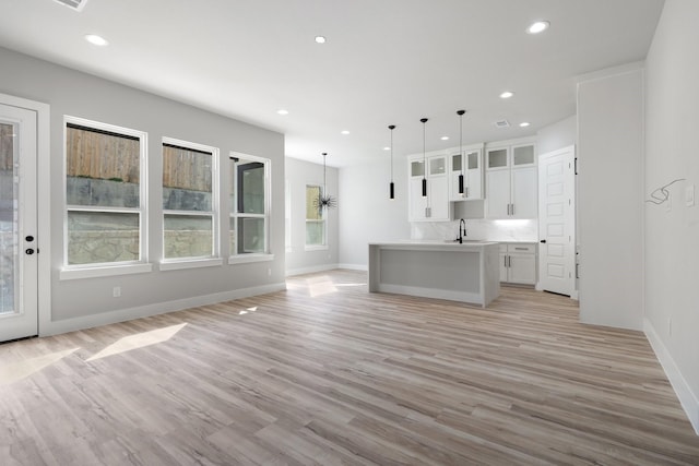 kitchen with white cabinetry, a kitchen island with sink, hanging light fixtures, and light hardwood / wood-style flooring