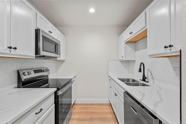 kitchen with sink, light hardwood / wood-style flooring, appliances with stainless steel finishes, white cabinetry, and light stone counters