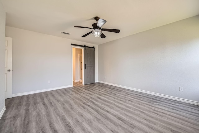 unfurnished bedroom with a barn door, light wood-type flooring, and ceiling fan