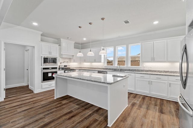 kitchen featuring appliances with stainless steel finishes, white cabinetry, a center island, tasteful backsplash, and decorative light fixtures