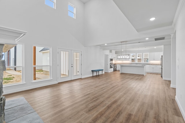 unfurnished living room featuring sink, crown molding, a towering ceiling, light hardwood / wood-style floors, and french doors