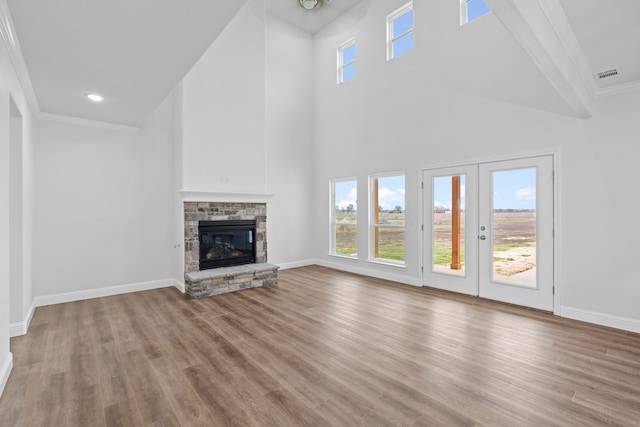 unfurnished living room featuring french doors, crown molding, a stone fireplace, and light hardwood / wood-style flooring