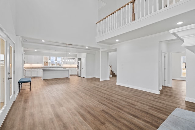 unfurnished living room featuring hardwood / wood-style flooring, crown molding, a high ceiling, and sink