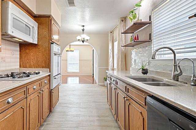 kitchen featuring sink, tasteful backsplash, decorative light fixtures, a chandelier, and white appliances