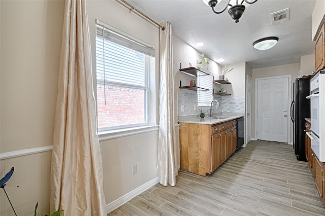 kitchen featuring sink, decorative backsplash, light hardwood / wood-style flooring, and black appliances