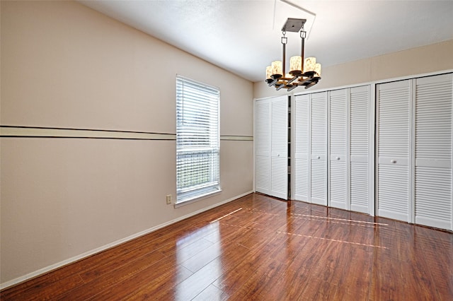 unfurnished bedroom with two closets, an inviting chandelier, and dark hardwood / wood-style flooring