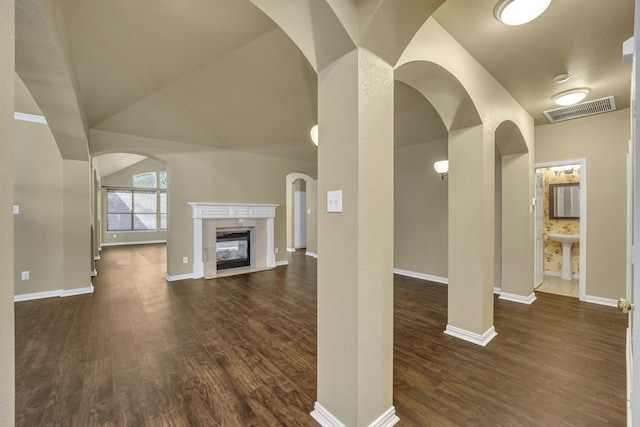 unfurnished living room featuring dark wood finished floors, a fireplace, and arched walkways