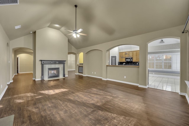 unfurnished living room with dark wood-type flooring, ceiling fan, a tiled fireplace, and high vaulted ceiling