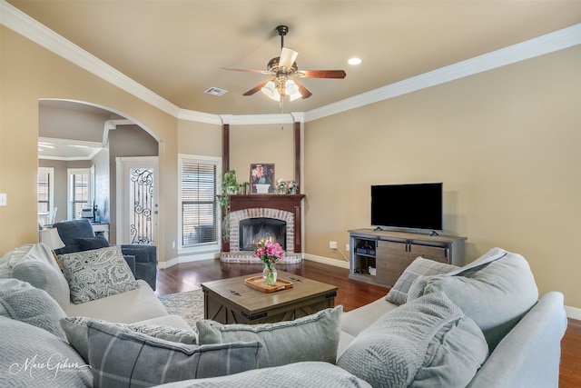 living room with ornamental molding, a brick fireplace, ceiling fan, and dark hardwood / wood-style flooring