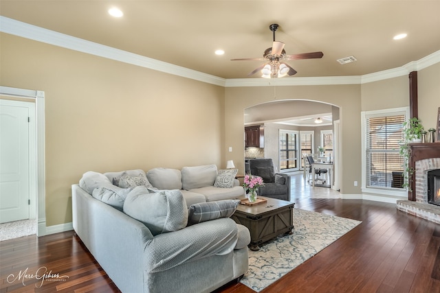 living room featuring dark wood-type flooring, ornamental molding, and a brick fireplace