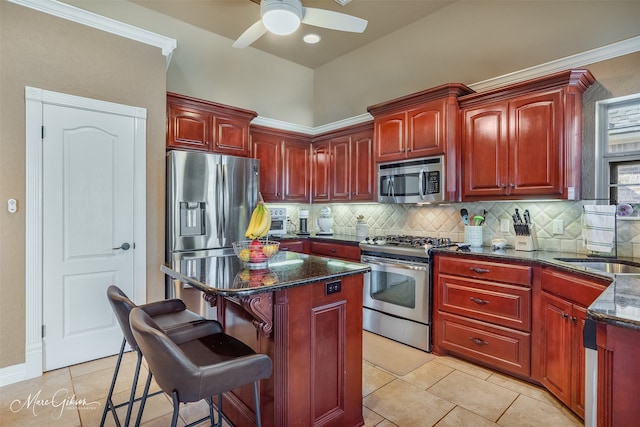 kitchen featuring light tile patterned flooring, a breakfast bar area, dark stone countertops, stainless steel appliances, and decorative backsplash