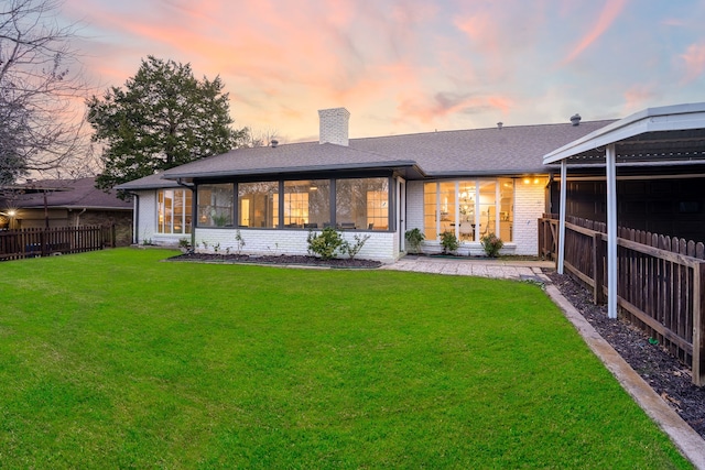 back house at dusk featuring a lawn