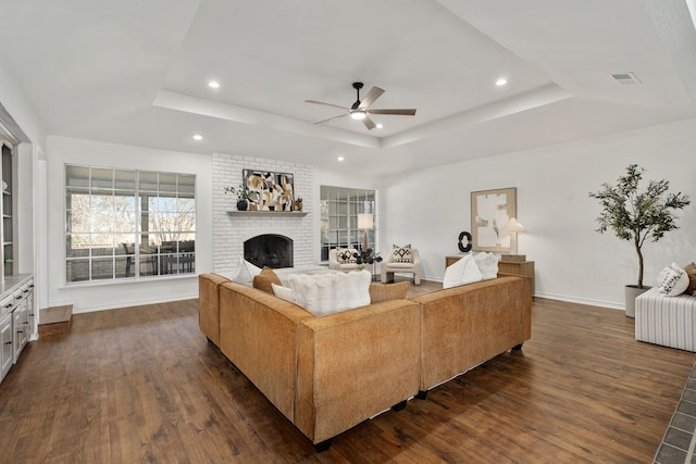 living room with a raised ceiling, dark wood-type flooring, and a fireplace