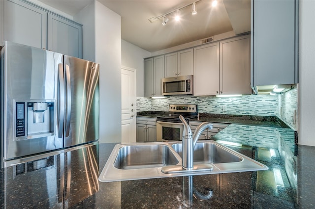 kitchen featuring rail lighting, tasteful backsplash, dark stone countertops, gray cabinets, and stainless steel appliances