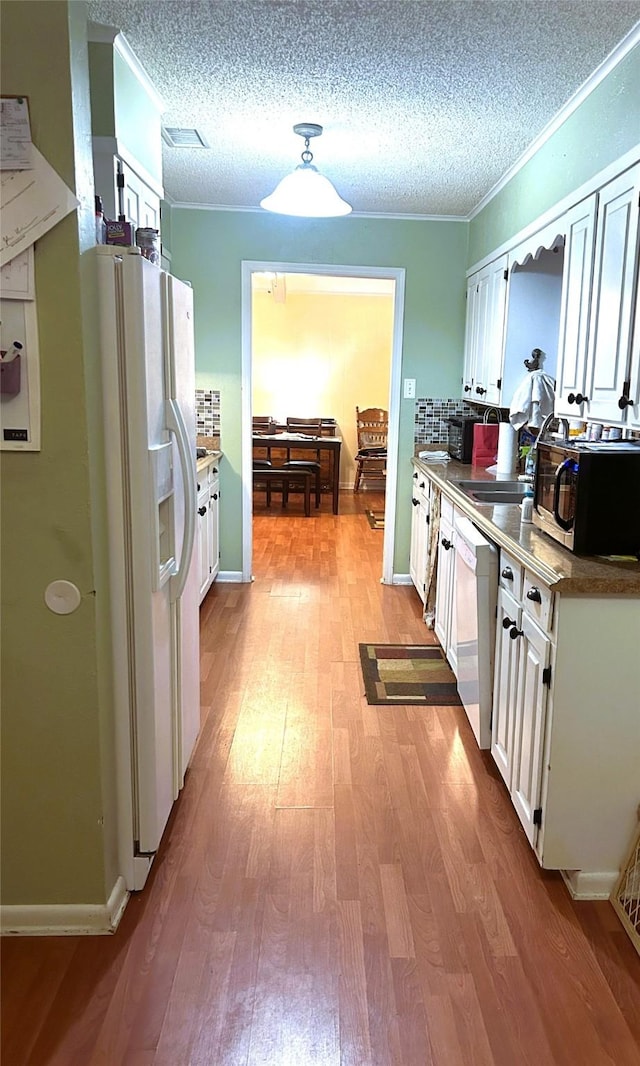 kitchen featuring white cabinetry, light hardwood / wood-style flooring, a textured ceiling, ornamental molding, and white appliances