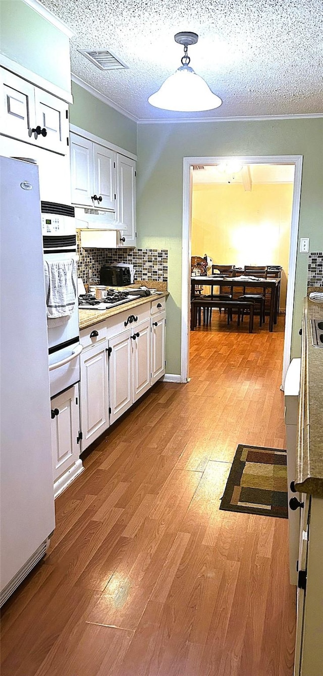 kitchen featuring white appliances, a textured ceiling, decorative backsplash, and white cabinets