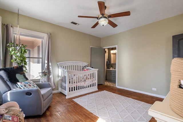 bedroom featuring hardwood / wood-style flooring, a nursery area, connected bathroom, and ceiling fan