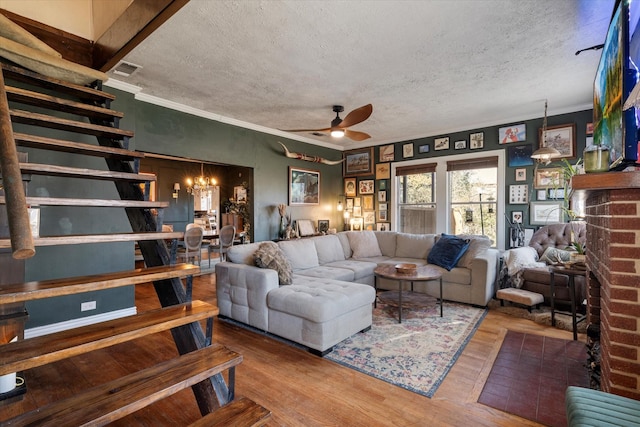 living room featuring hardwood / wood-style floors, ornamental molding, a textured ceiling, a brick fireplace, and ceiling fan with notable chandelier