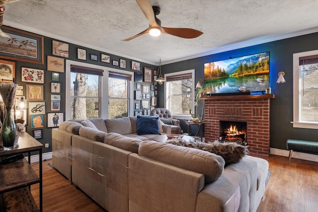 living room with a textured ceiling, ornamental molding, hardwood / wood-style flooring, ceiling fan, and a fireplace