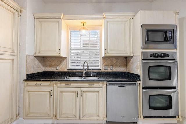 kitchen with pendant lighting, sink, dark stone counters, stainless steel appliances, and cream cabinetry