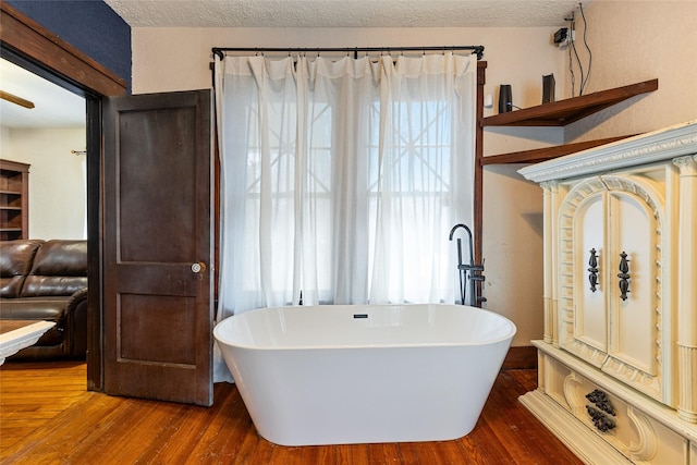 bathroom with hardwood / wood-style floors, a bath, and a textured ceiling