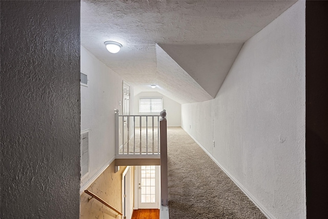 corridor with a healthy amount of sunlight, carpet flooring, vaulted ceiling, and a textured ceiling