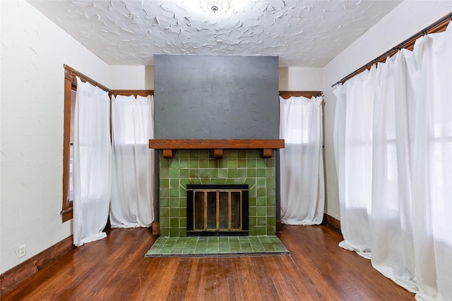 unfurnished living room featuring dark hardwood / wood-style floors, a tiled fireplace, and a textured ceiling