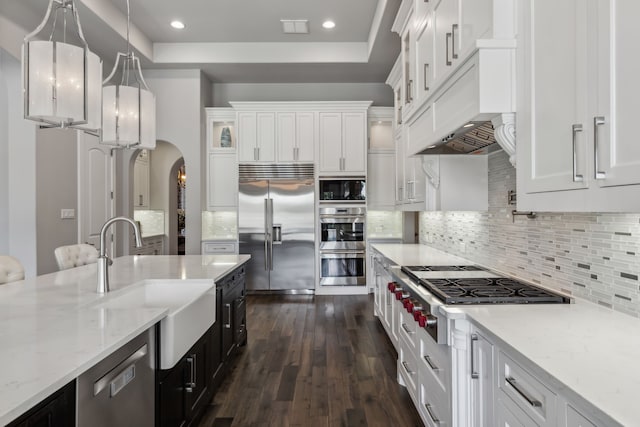 kitchen featuring hanging light fixtures, sink, built in appliances, and white cabinets