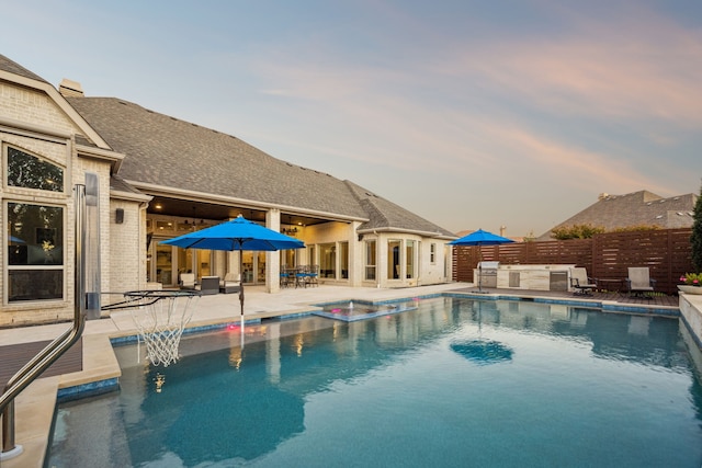 pool at dusk with a patio and area for grilling