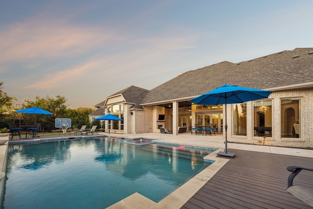 pool at dusk with a fireplace and a patio area