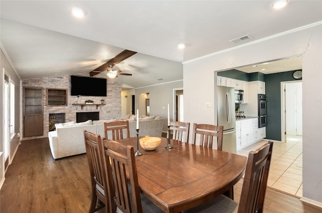 dining space featuring a stone fireplace, vaulted ceiling with beams, ornamental molding, hardwood / wood-style flooring, and ceiling fan