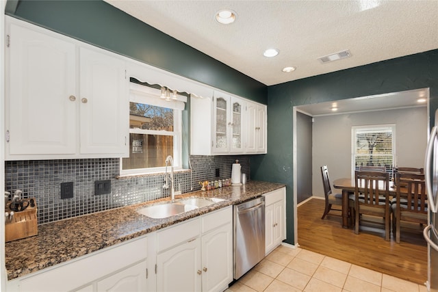 kitchen featuring sink, dishwasher, white cabinets, light tile patterned flooring, and dark stone counters