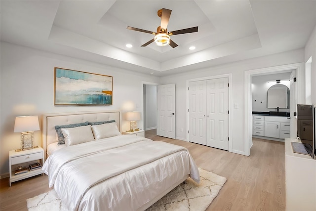 bedroom with a tray ceiling, light wood-type flooring, ceiling fan, and ensuite bathroom