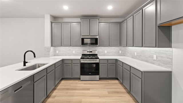 kitchen with tasteful backsplash, sink, gray cabinetry, stainless steel appliances, and light wood-type flooring