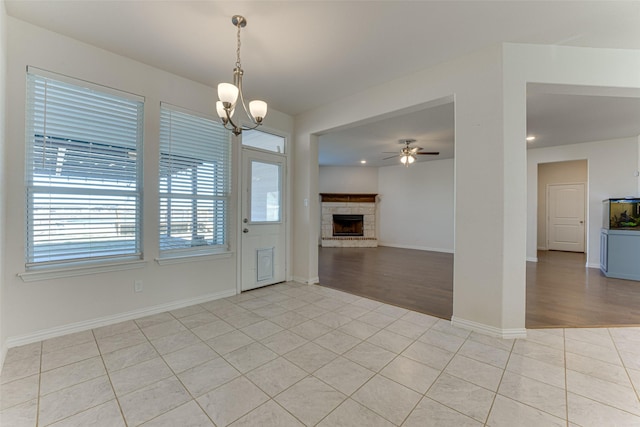 unfurnished living room featuring light tile patterned flooring, a stone fireplace, and ceiling fan with notable chandelier