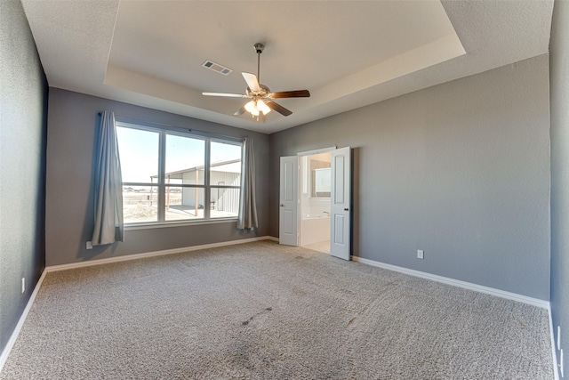 unfurnished bedroom featuring light carpet, a tray ceiling, ensuite bath, and ceiling fan