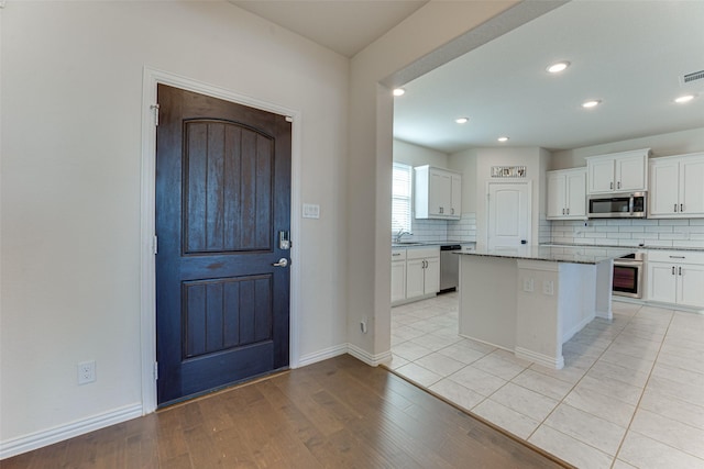 kitchen with decorative backsplash, a center island, white cabinets, and appliances with stainless steel finishes