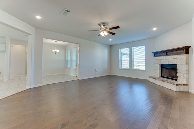 unfurnished living room featuring a stone fireplace, ceiling fan with notable chandelier, and hardwood / wood-style flooring