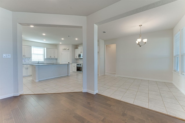 kitchen with white cabinetry, backsplash, light hardwood / wood-style floors, stainless steel appliances, and an inviting chandelier