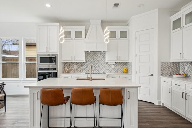 kitchen with a breakfast bar area, an island with sink, custom range hood, and appliances with stainless steel finishes