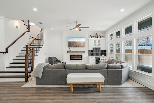 living area featuring a ceiling fan, wood finished floors, stairs, a glass covered fireplace, and recessed lighting