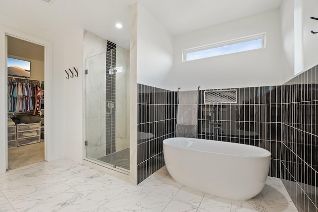 full bathroom featuring a walk in closet, a freestanding bath, a stall shower, marble finish floor, and tile walls