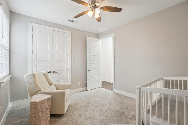 carpeted bedroom featuring visible vents, a crib, a ceiling fan, a closet, and baseboards